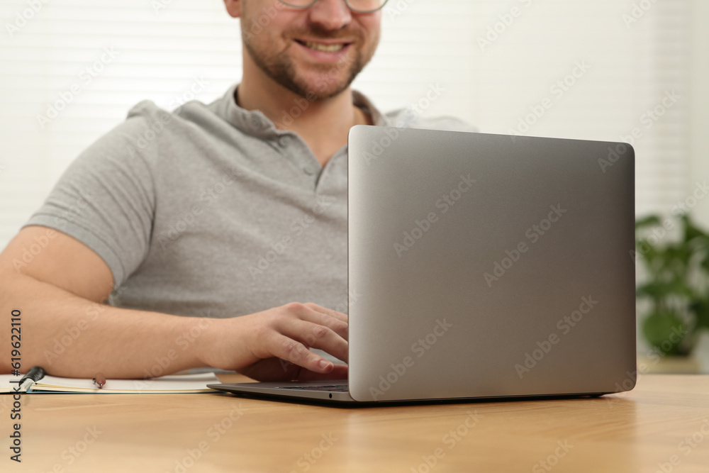 Man working with laptop at wooden table indoors, closeup Man working with laptop at wooden table indoors, closeup