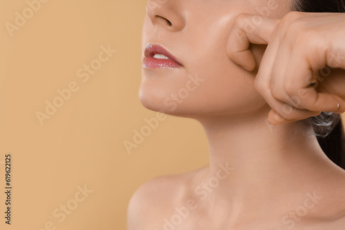 Young woman massaging her face on beige background, closeup. Space for text