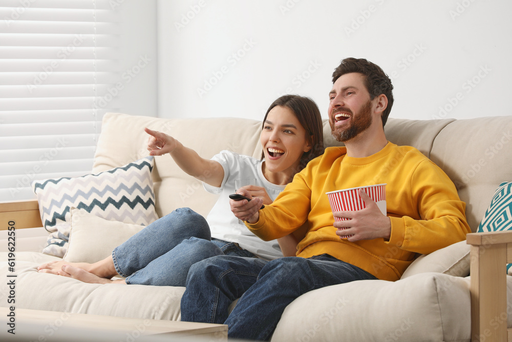 Happy couple watching TV with popcorn on sofa at home