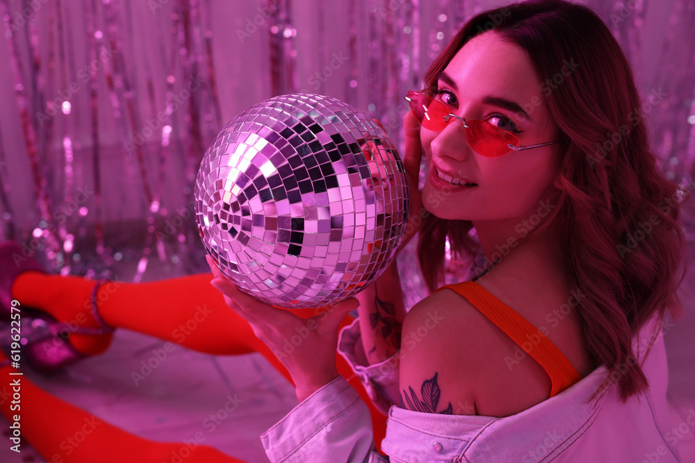 Naklejka premium Beautiful woman in stylish outfit with disco ball at party indoors, toned in pink