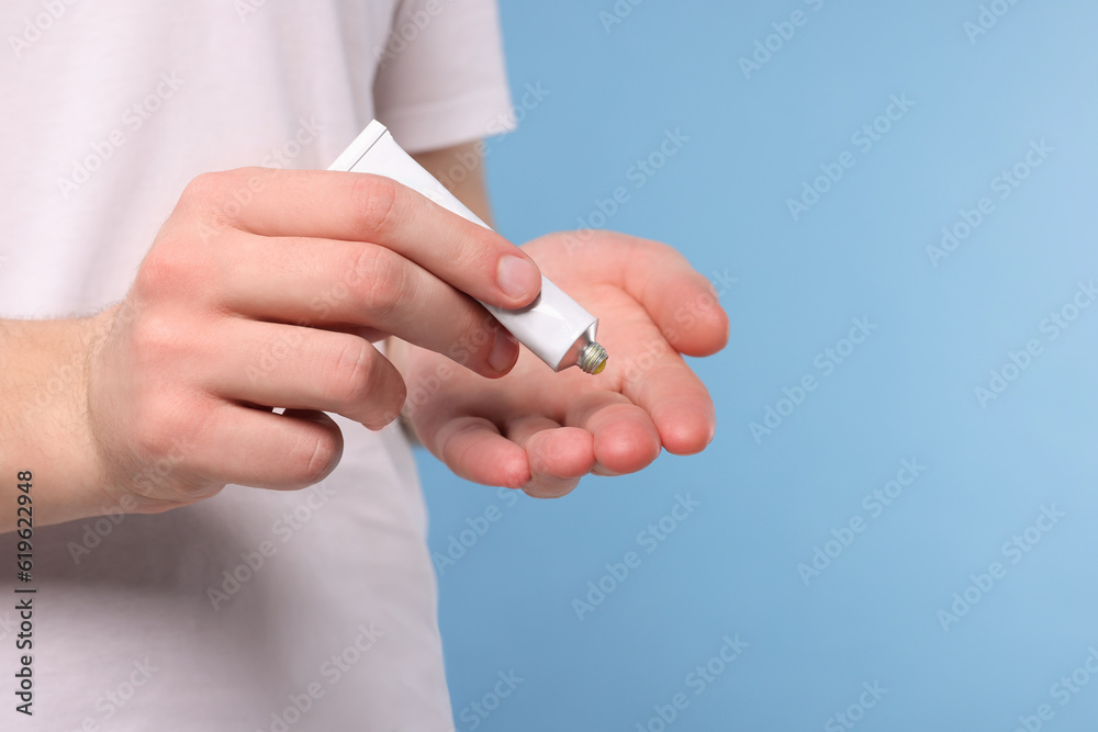 Man applying ointment from tube onto his hand on light blue background, closeup. Space for text Man applying ointment from tube onto his hand on light blue background, closeup. Space for text