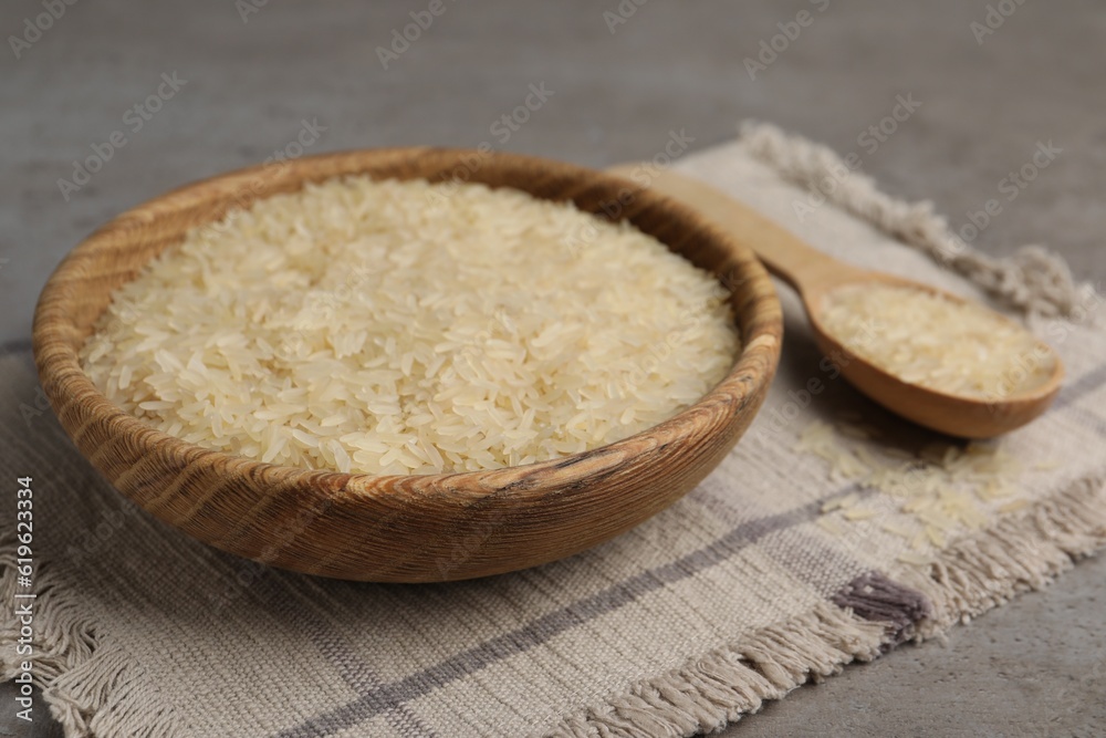 Bowl and spoon of raw rice on grey table, closeup Bowl and spoon of raw rice on grey table, closeup