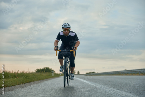 Dynamic image of young bearded man , cyclist in helmet riding bike on empty road in the evening. Active weekends. Concept of sport, hobby, leisure activity, training, health, speed, endurance, ad