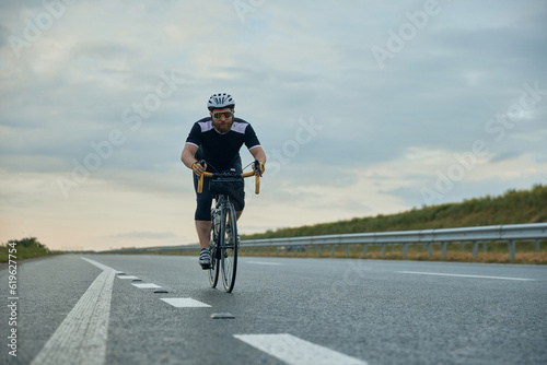 Dynamic image of young, sportive, bearded man, cyclist in helmet riding bicycle on empty road in the evening. Concept of sport, hobby, leisure activity, training, health, speed, endurance, ad