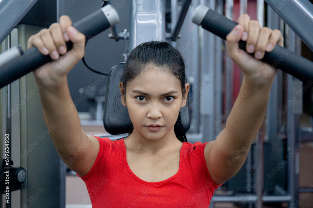 Fototapeta premium Young asian woman workout with strength training and determination with fitness gym machines, energetic asia woman exercise with motivation in fitness, sport and health, strong and flexibility.