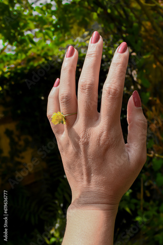 The hand of a woman wearing a flower as a ring on her finger.