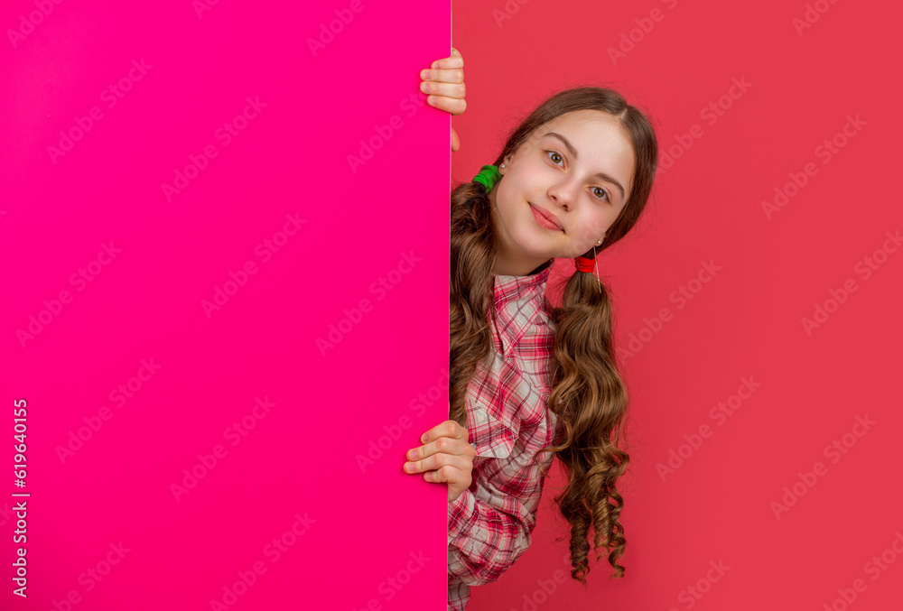 smiling teen kid behind blank pink paper with copy space for advertisement
