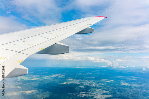 View of airplane wing, blue skies and green land during landing. Airplane window view.