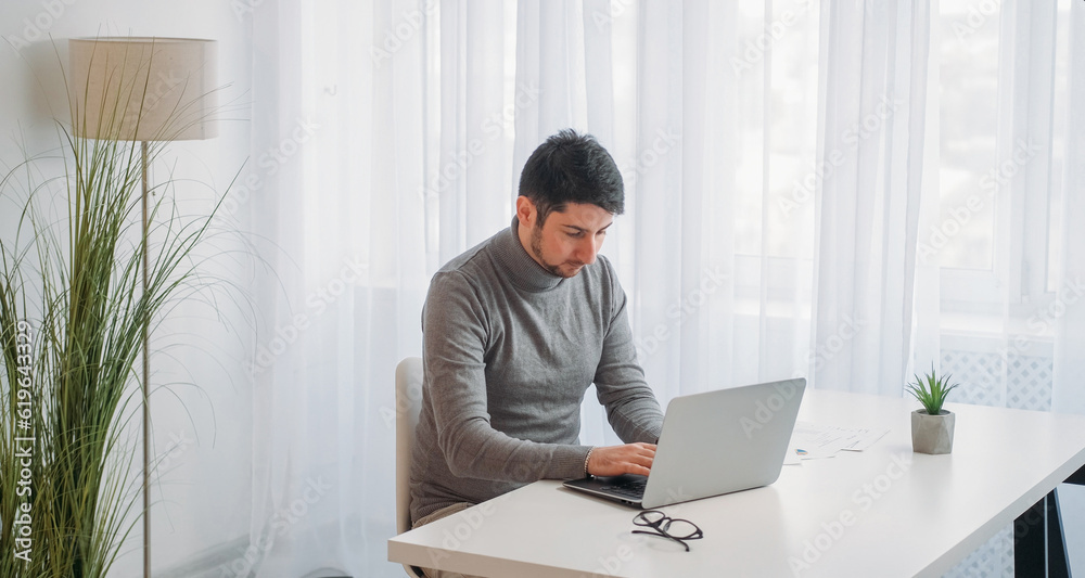 Computer job. Office work. Data analysis. Tired tensed focused business man chatting typing at laptop at workplace desktop with documents free space.