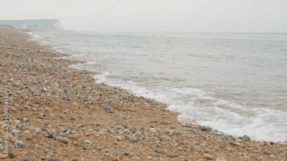 Slowmotion shot of the pebble rocky coast of Seaford with rocks in the foreground and white chalk cliffs in the background. Gloomy grey weather. Shot during sunrise in 4k, 60p. Slowmotion shot of the pebble rocky coast of Seaford with rocks in the foreground and white chalk cliffs in the background. Gloomy grey weather. Shot during sunrise in 4k, 60p.