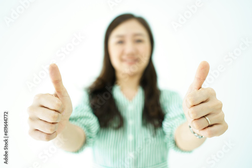 Happy cheerful Asian young adult woman showing thumb up and smiles to camera, Asian woman in action portrait on white background.