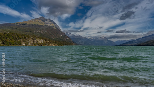 The beautiful emerald lake is surrounded by mountains. The waves are foaming on the pebbly shore. Blue sky with picturesque clouds. Tierra del Fuego National Park. Lago Roca. Argentina.