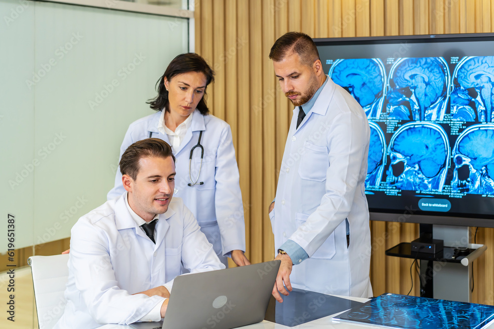 Team of three doctors discusses the results of an MRI scan of the patient's head in the consulting room of modern hospital, physician discussing about treatment for patient looking in laptop