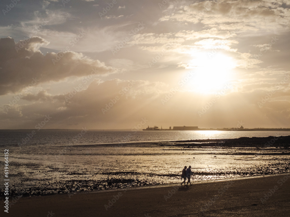 Sunrise over industrial site at Barney Point, Gladstone, Queensland, with 2 people walking on the beach at low tide.