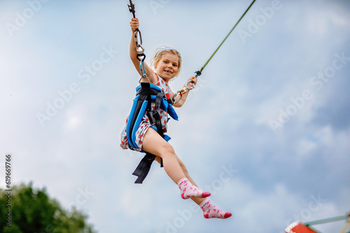 Little preschool girl enjoying jumping with trampoline jumping rope. Happy child in amusement park. Family activity