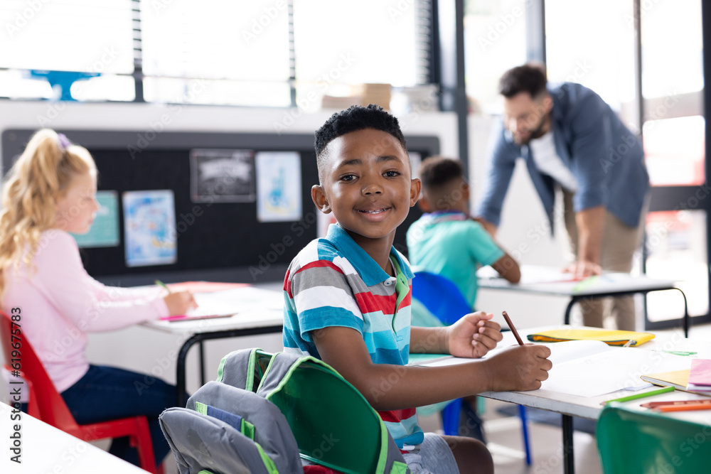 Obraz premium Portrait of smiling african american boy at desk in elementary school classroom, copy space