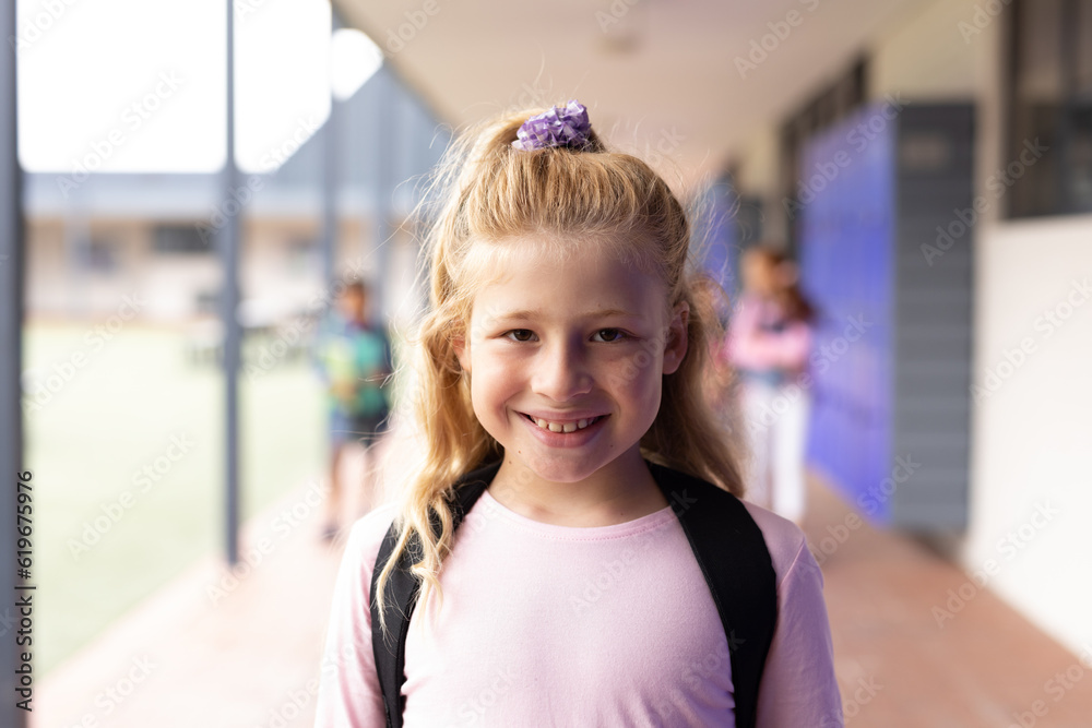Portrait of smiling caucasian schoolgirl in elementary school corridor, with copy space