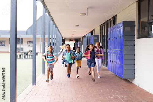 Diverse, happy children with schoolbags running in elementary school corridor, copy space