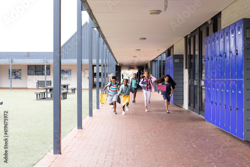 Happy, diverse children running in elementary school corridor, copy space