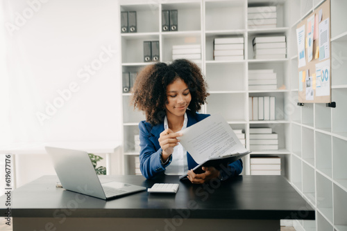 Beautiful African woman typing on tablet and laptop while sitting at the working wooden table modern office