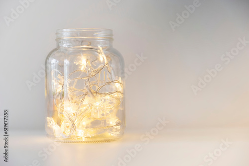 Warm glowing christmas lights in a glass jar on a white background