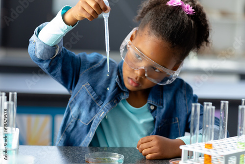 Biracial schoolgirl in safety glasses using pipette in science class with copy space