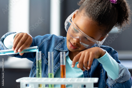 Happy biracial schoolgirl in safety glasses doing experiment in science class with copy space