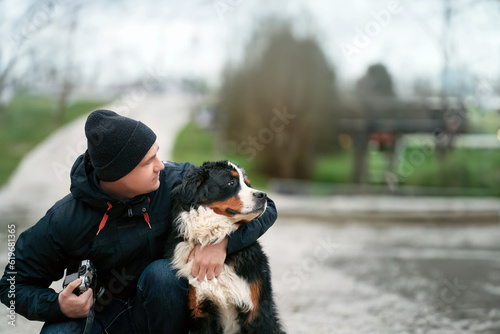 Happy owner and young Bernese puppy. Playful Adorable Bernese Mountain Dog and a Man Portrait in the Swiss Alps