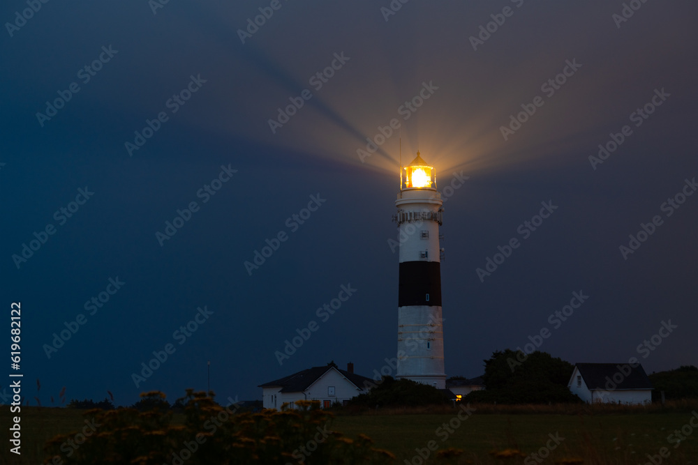 Kampen lighthouse on Sylt island Germany in blue hour twilight. Black and white tower on a misty evening with rotating guiding flash light for North Sea navigation. Orientation for ships and landmark.