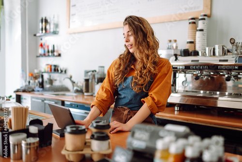 Beautiful woman owner stands behind the counter of a coffee shop. A barista with a digital tablet takes an order. Business concept. Takeaway food.