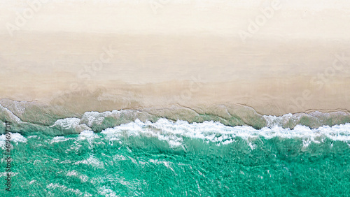 Beautiful quiet white beach background with emerald green ocean waters. Aerial view from above of sea and sand.