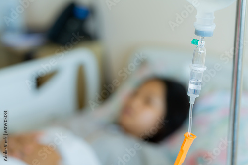Fotografia Young patient asian woman lying on the bed in hospital with IV saline drip to the back of the hand, teenager sick in hospital, Selective focus, healthcare, and health insurance concept