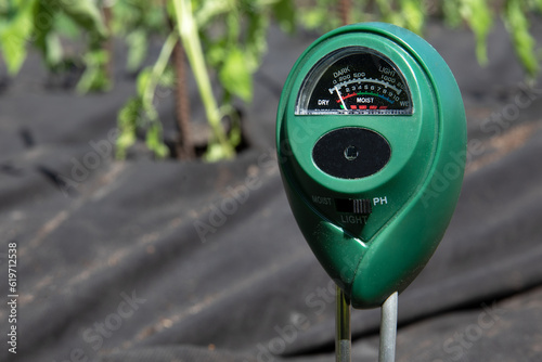 Ph meter for measuring the level of alkali in the ground for plants. A device for monitoring the composition of the soil stuck into the ground and standing on a spandbond in a greenhouse photo