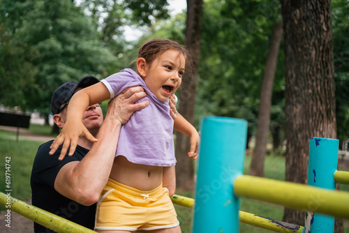 Father with child girl doing pull-ups on workout outdoor area. Healthy active lifestyle, happy family time. Modern fatherhood concept 