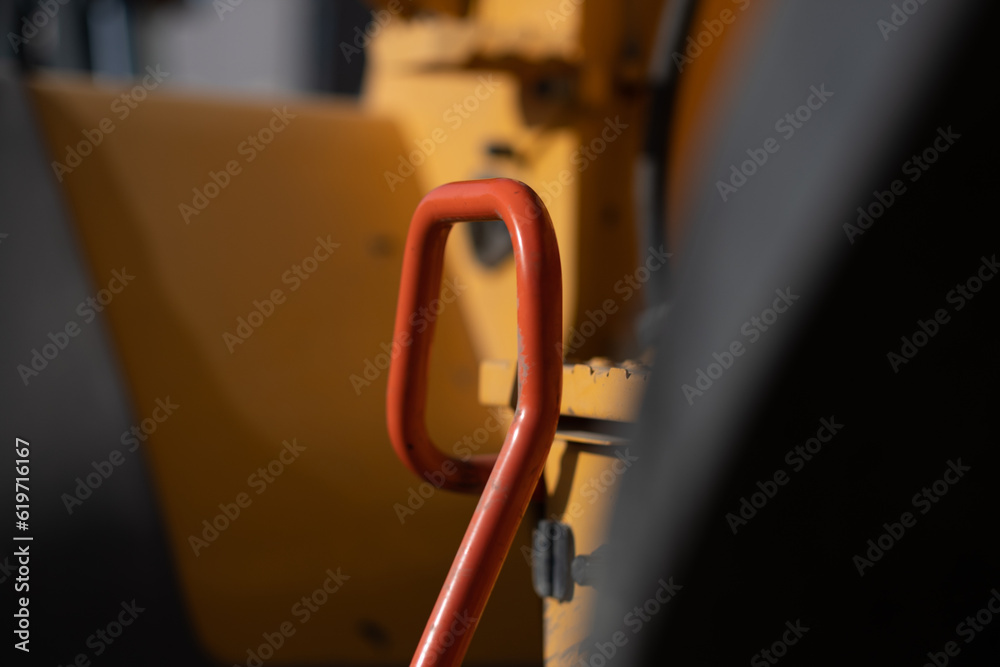 Closeup of a red handrail on a piece of bright orange machinery at a construction site.