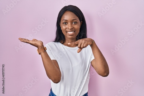African young woman wearing casual white t shirt amazed and smiling to the camera while presenting with hand and pointing with finger.