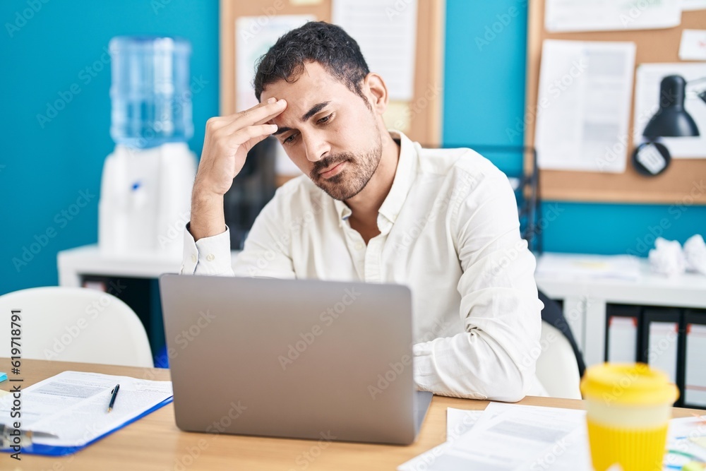 Fototapeta premium Young hispanic man business worker stressed using laptop at office
