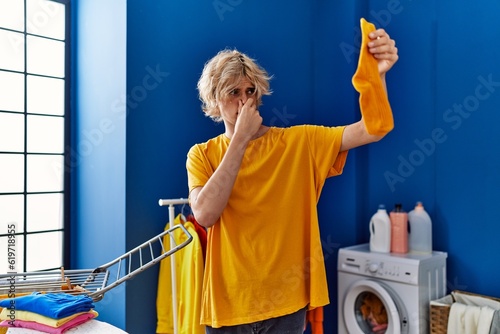 Young blond man holding dirty sock at laundry room photo