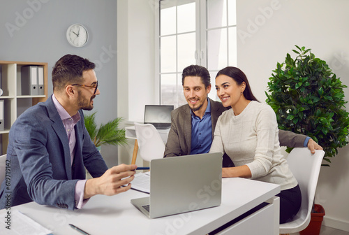 Portrait of happy caucasian couple sitting with a business broker or insurance agent showing project on a laptop screen. Clients having consultation with a man realtor or financial advisor at office.