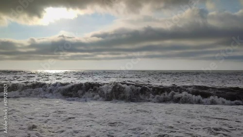 A powerful storm brews over the Sea, with dramatic waves splashing against the coastline and strong winds stirring the seascape. Dark clouds fill the sky, creating a dramatic, stormy atmosphere.
