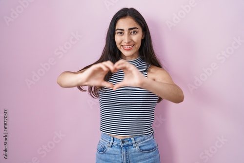 Young teenager girl wearing casual striped t shirt smiling in love doing heart symbol shape with hands. romantic concept. © Krakenimages.com