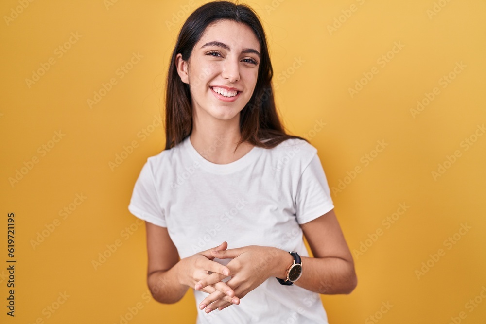 Obraz premium Young beautiful woman standing over yellow background hands together and fingers crossed smiling relaxed and cheerful. success and optimistic