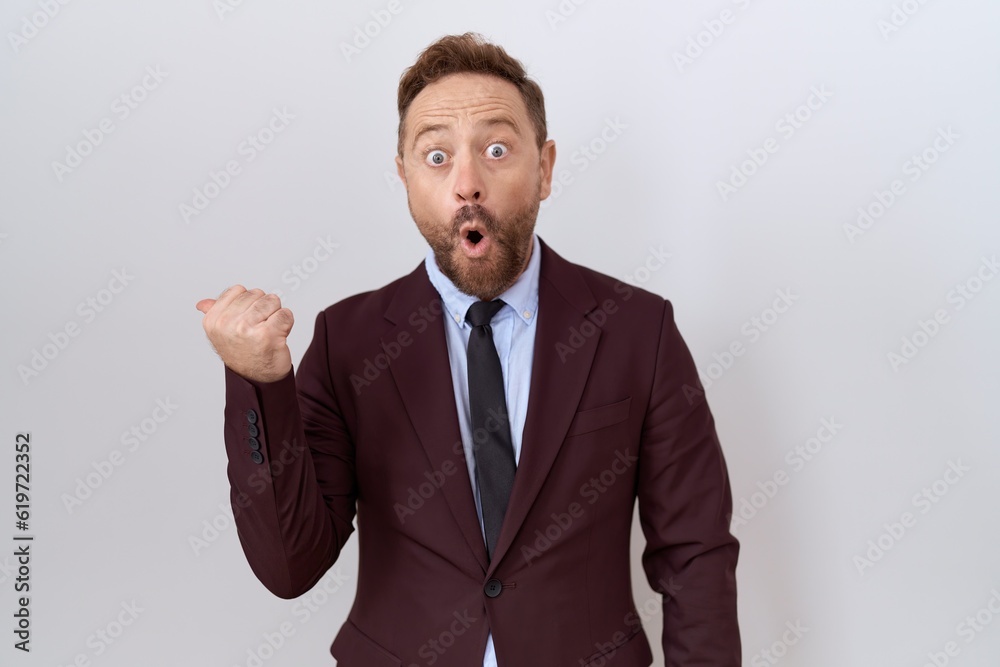 Middle age business man with beard wearing suit and tie surprised pointing with hand finger to the side, open mouth amazed expression. Middle age business man with beard wearing suit and tie surprised pointing with hand finger to the side, open mouth amazed expression.