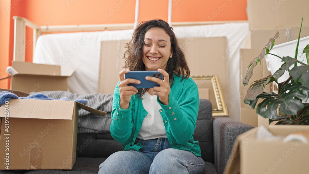 Young beautiful hispanic woman playing video game sitting on sofa at new home Young beautiful hispanic woman playing video game sitting on sofa at new home