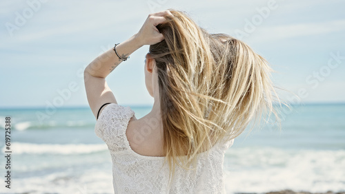 Young blonde woman tourist touching hair standing backwards at beach