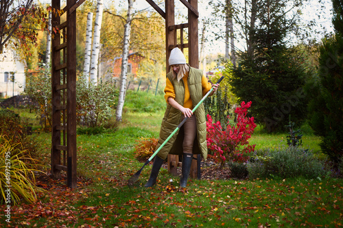 Fotografia seasonal autumn garden work. Woman gardener raking fall leaves