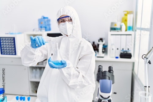Young blonde woman scientist wearing security uniform pouring liquid on test tube at laboratory