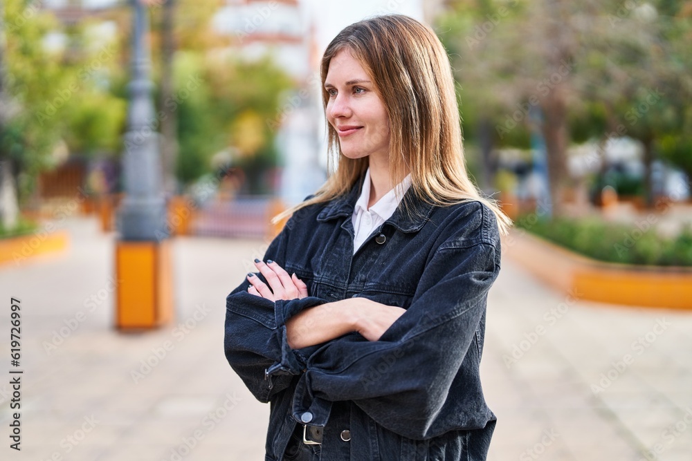 Young blonde woman standing with crossed arms looking to the side at park Young blonde woman standing with crossed arms looking to the side at park