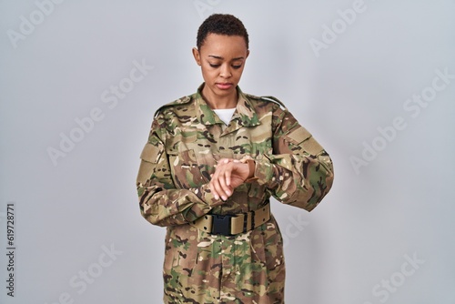 Beautiful african american woman wearing camouflage army uniform checking the time on wrist watch, relaxed and confident