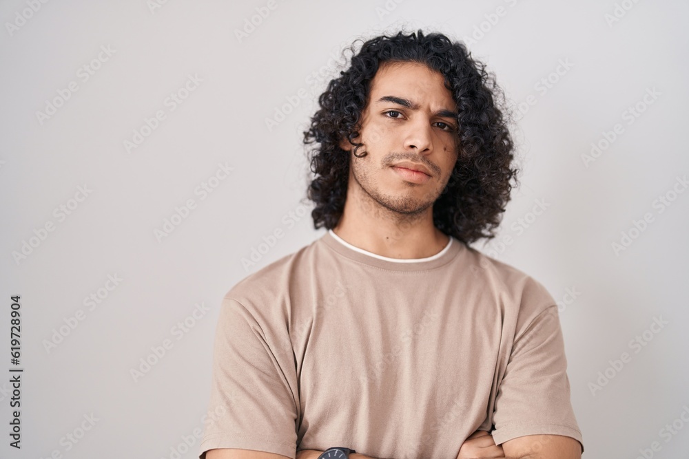 Obraz premium Hispanic man with curly hair standing over white background skeptic and nervous, disapproving expression on face with crossed arms. negative person.